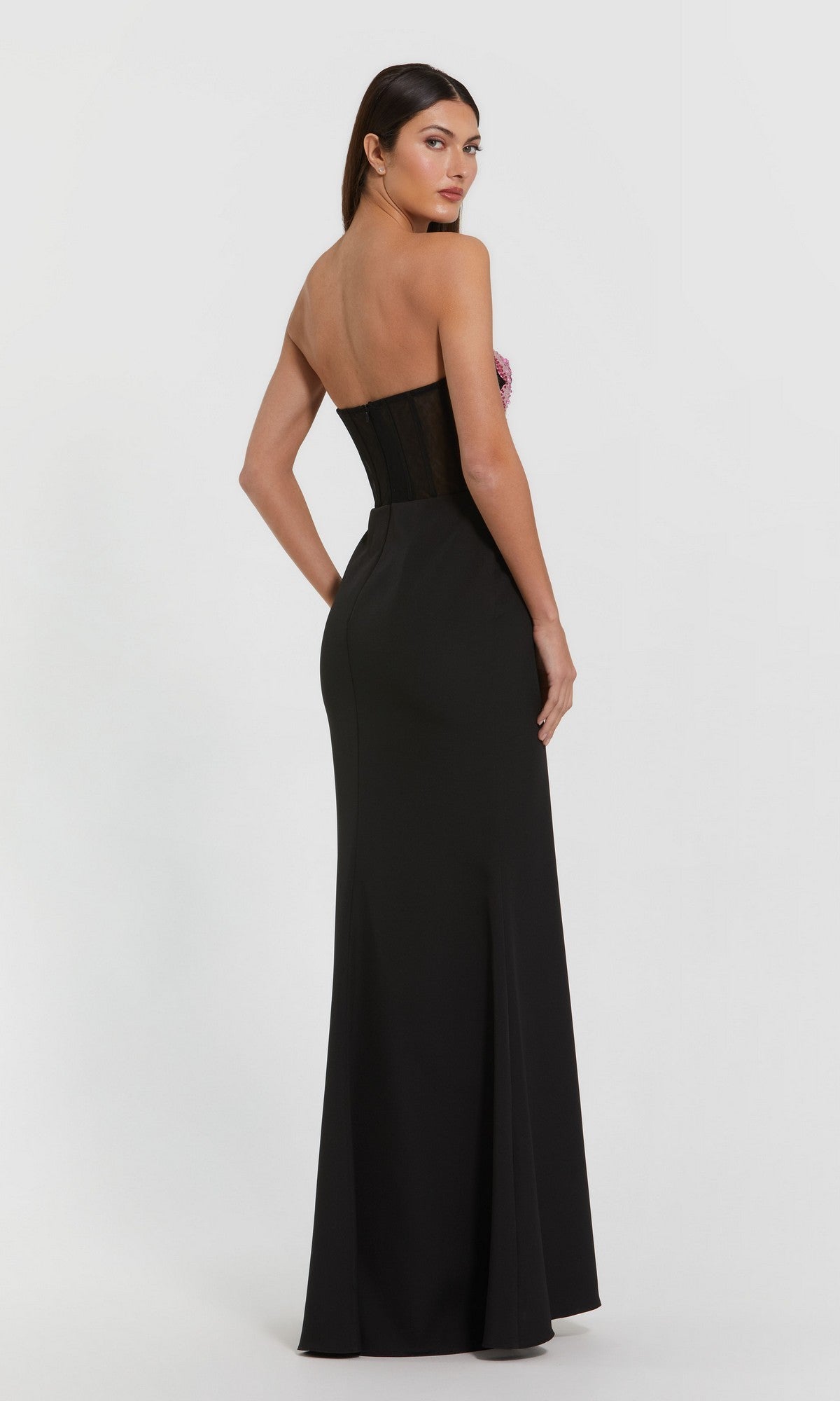 Woman in the Mac Duggal 20682 long formal dress, featuring a strapless fitted bodice and flowing skirt, stands looking over her shoulder against a plain background—the ideal special occasion look.